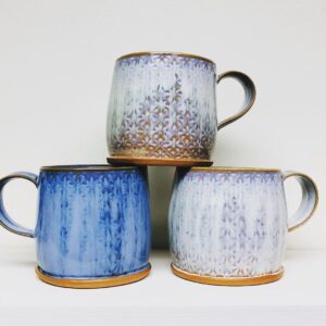 Three mugs, one blue two white, stacked in a pyramid.