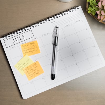Above view of a smartphone, pencil holder, calendar with sticky notes on a desk.