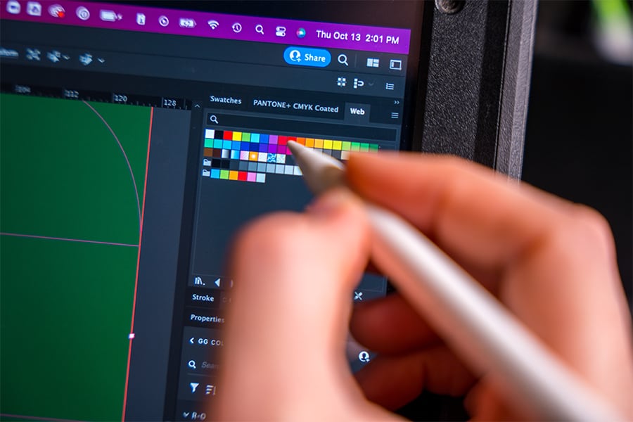 5050-fpo-office-brainstorming Up-close shot of a hand holding a stylus hovering over different colors while designing graphics in Adobe Photoshop.