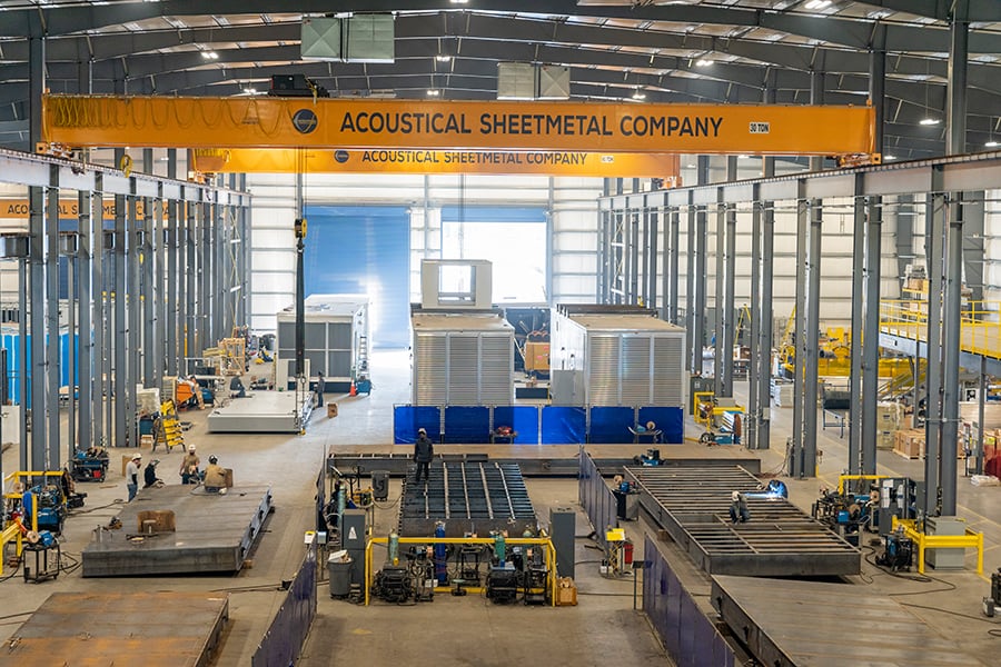 The inside of the Acoustical Sheetmetal Company warehouse with various workers and enclosures being produced.