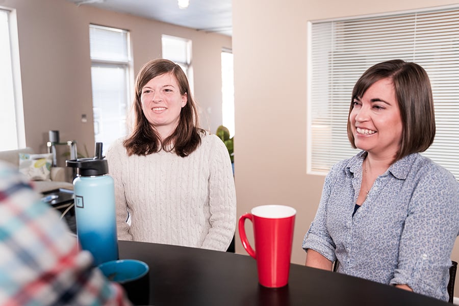 5050-fpo-office-brainstorming Two women and one man talking at a table with a water bottle and coffee mug